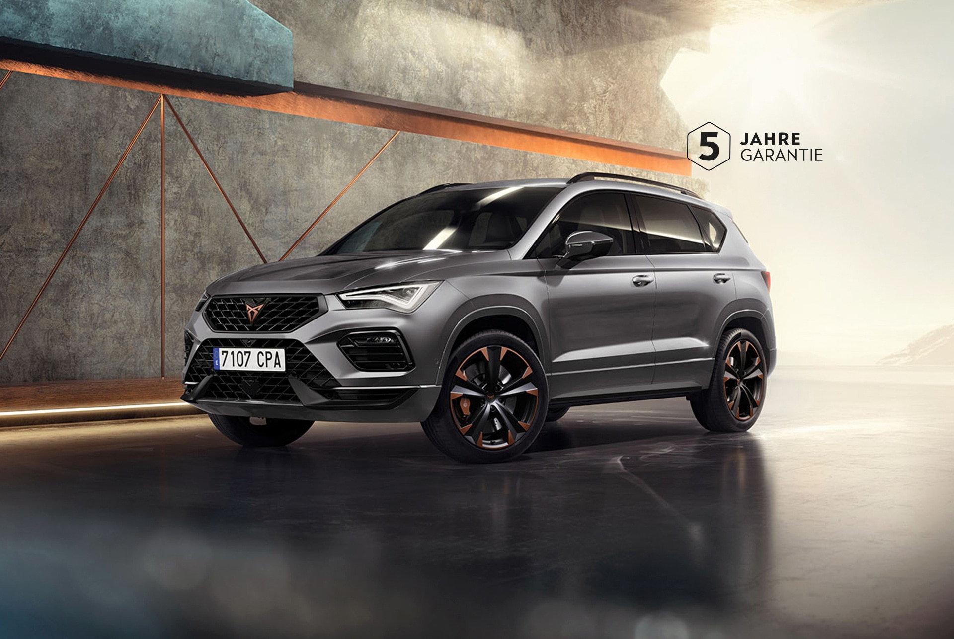 Ein CUPRA Ateca 2024 in Graphite Grey, ein sportlicher und kompakter SUV in einer modernen, industriellen Umgebung. Das Fahrzeugdesign zeichnet sich durch aerodynamische Linien, LED-Scheinwerfer und markante Leichtmetallräder mit Kupferakzenten aus. Der Hintergrund zeigt ein geometrisches Wanddesign, das im Kontrast zum eleganten Fahrzeugdesign steht.