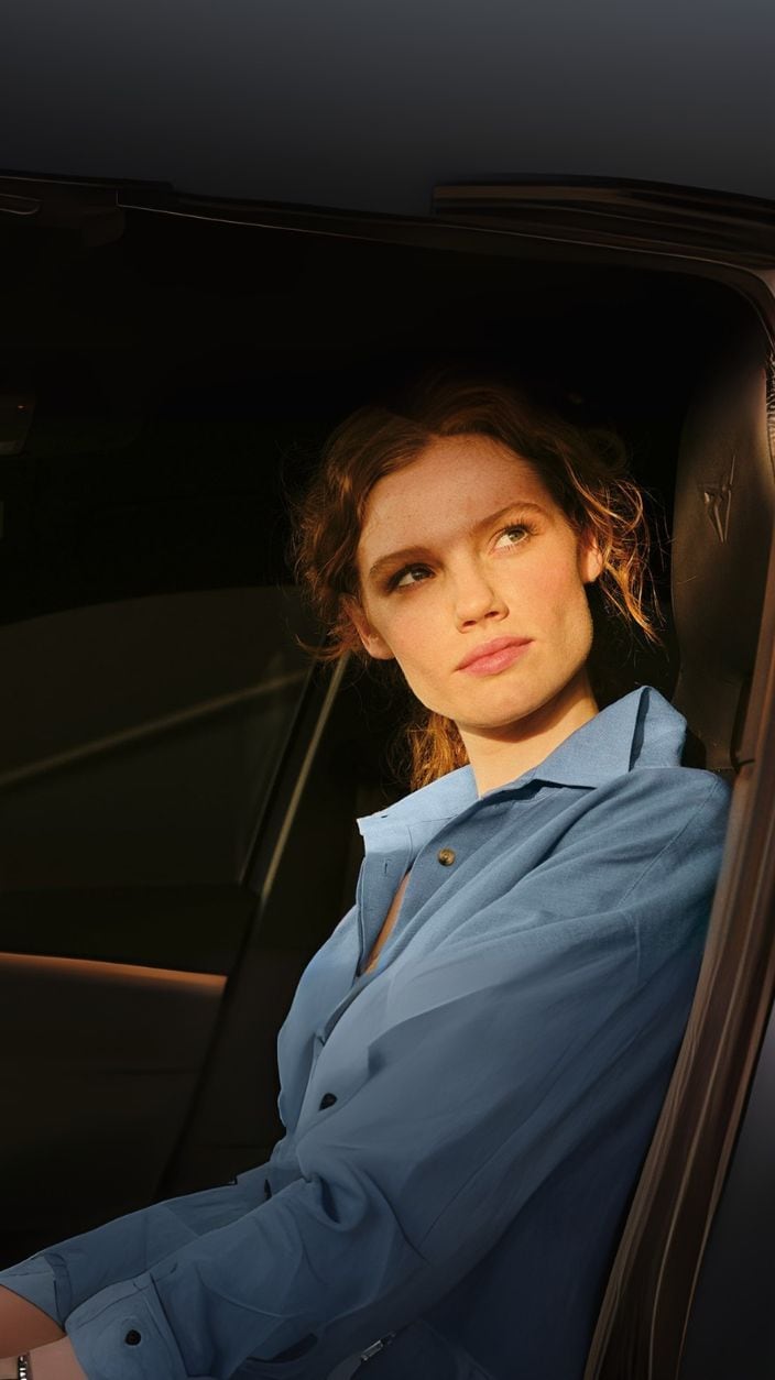 Eine junge Frau sitzt in Ihrem Auto und wird von der Sonne gekitzelt.