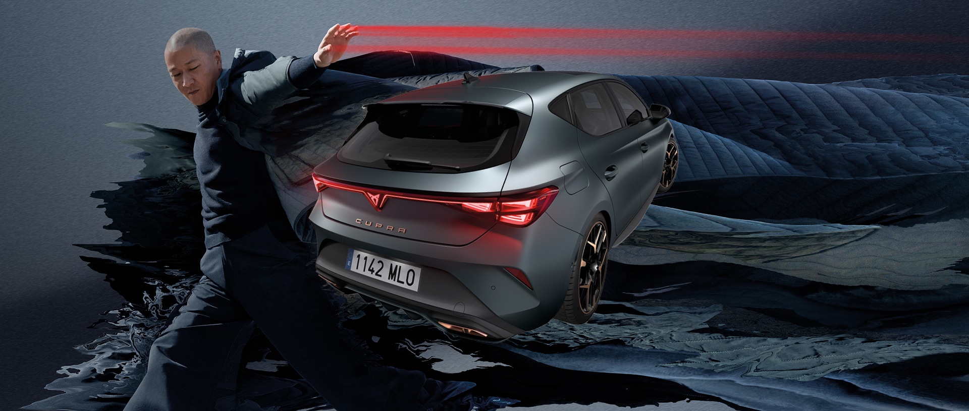 Der neue CUPRA Leon 2024 in enceladus grey matte mit kupferfarbenen Leichtmetallfelgen, geparkt auf glattem Beton unter einer architektonischen Struktur. Im Hintergrund das Stadtbild von Barcelona.
