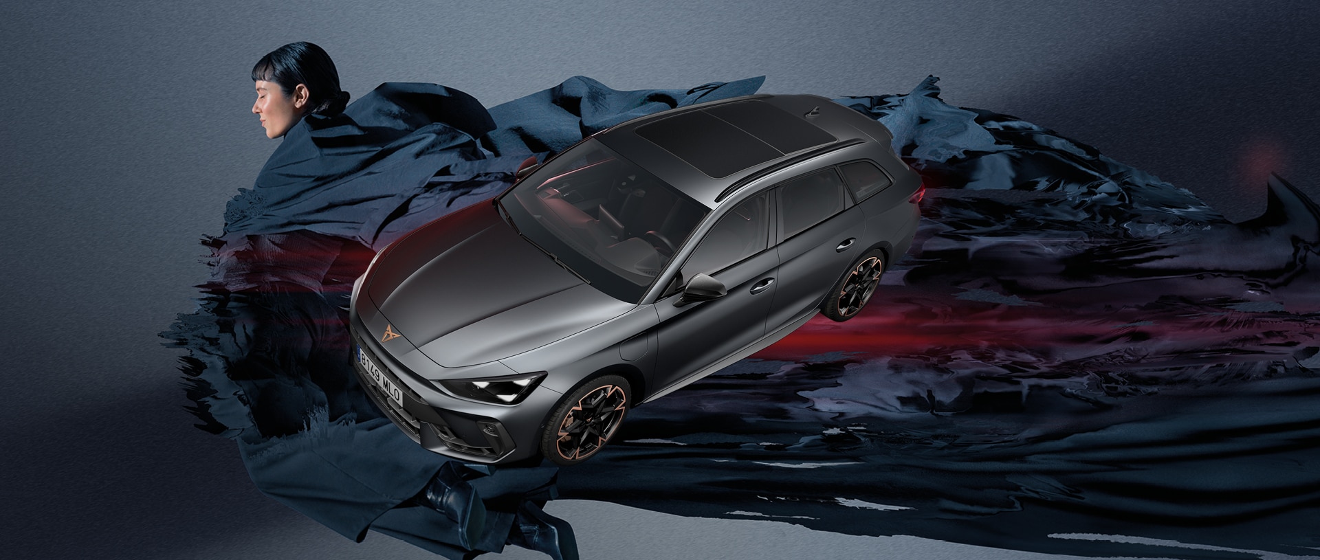 Weitwinkelansicht des sportlichen neuen CUPRA Leon Sportstourer 2024 Hybrid-Fahrzeugs in Matte Grey, parkiert im städtischen Umfeld vor grossen, an Gaudí erinnernden geometrischen Fenstern.  