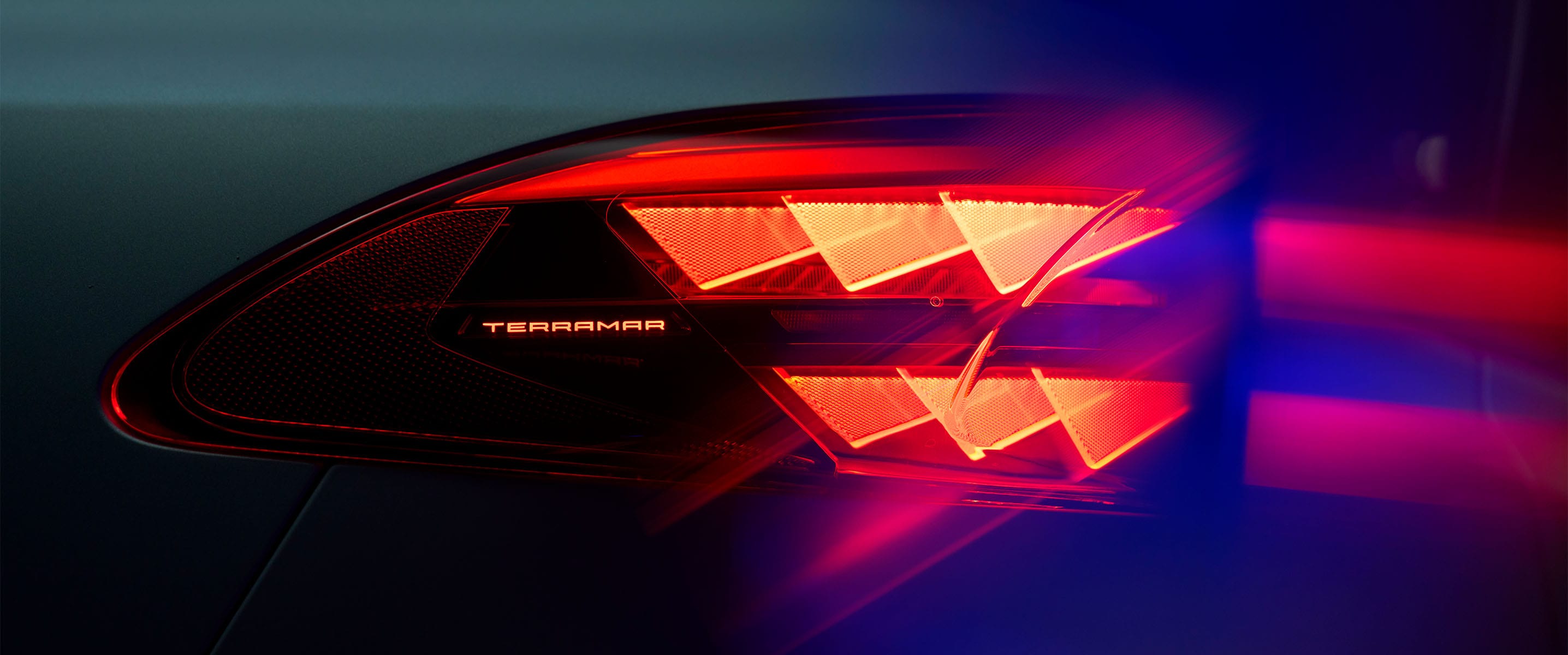 Nahaufnahme der Cupra Terramar-Rückleuchte mit beleuchtetem Modellnamen, die das charakteristische rote dreieckige Lichtmuster vor dunklem Hintergrund zeigt.