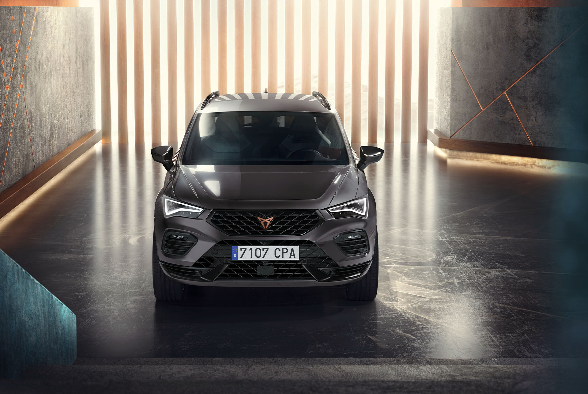 Una vista frontale della Cupra Ateca, un SUV grigio, in un ambiente moderno e illuminato. L'immagine mette in evidenza l'audace griglia anteriore, i fari a LED e il design elegante dell'auto. 