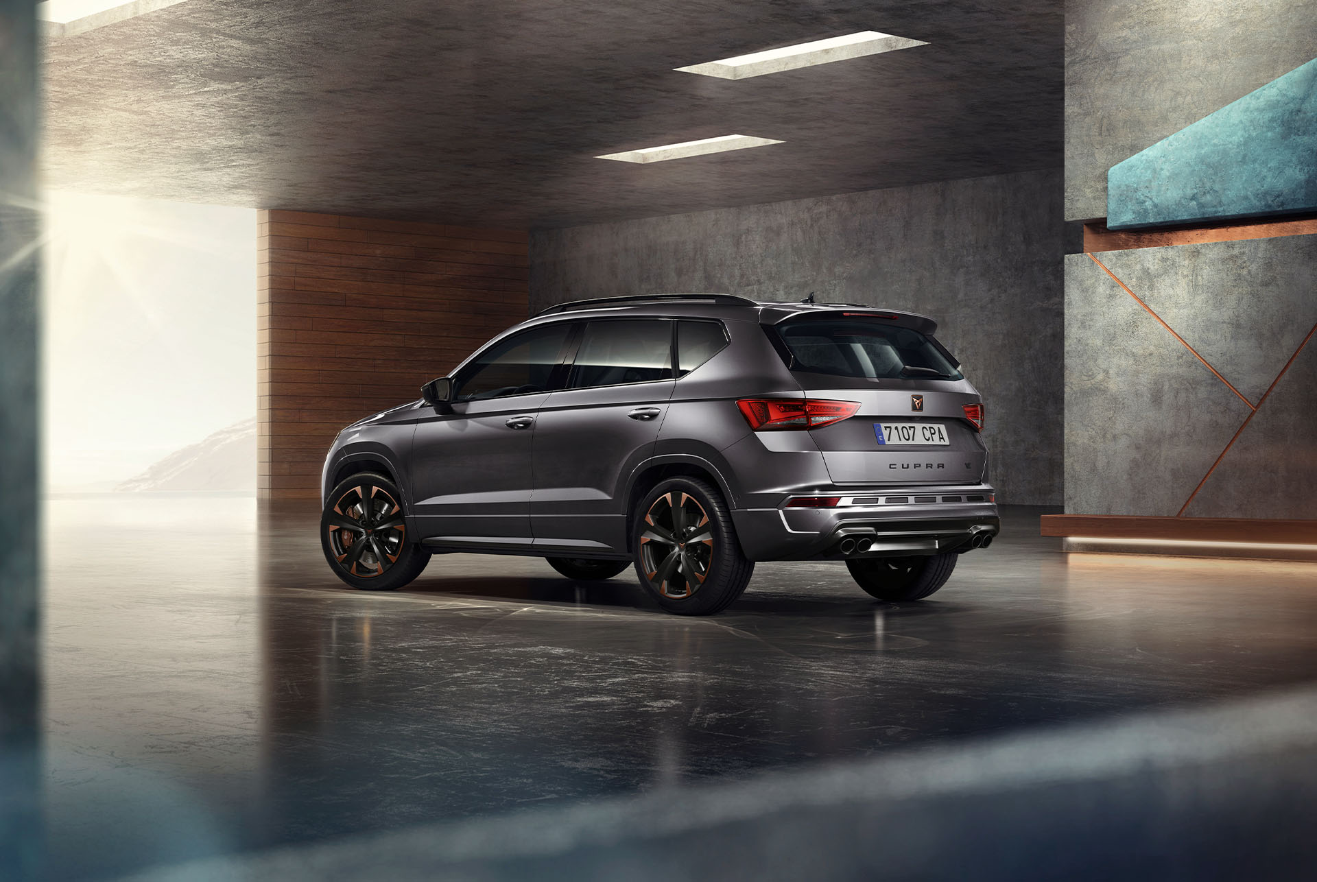 Un SUV CUPRA Ateca grigio viene raffigurato su uno sfondo bianco. La calandra pronunciata, i fari a LED e i cerchi in lega leggera con dettagli in rame sottolineano il design sportivo del veicolo.