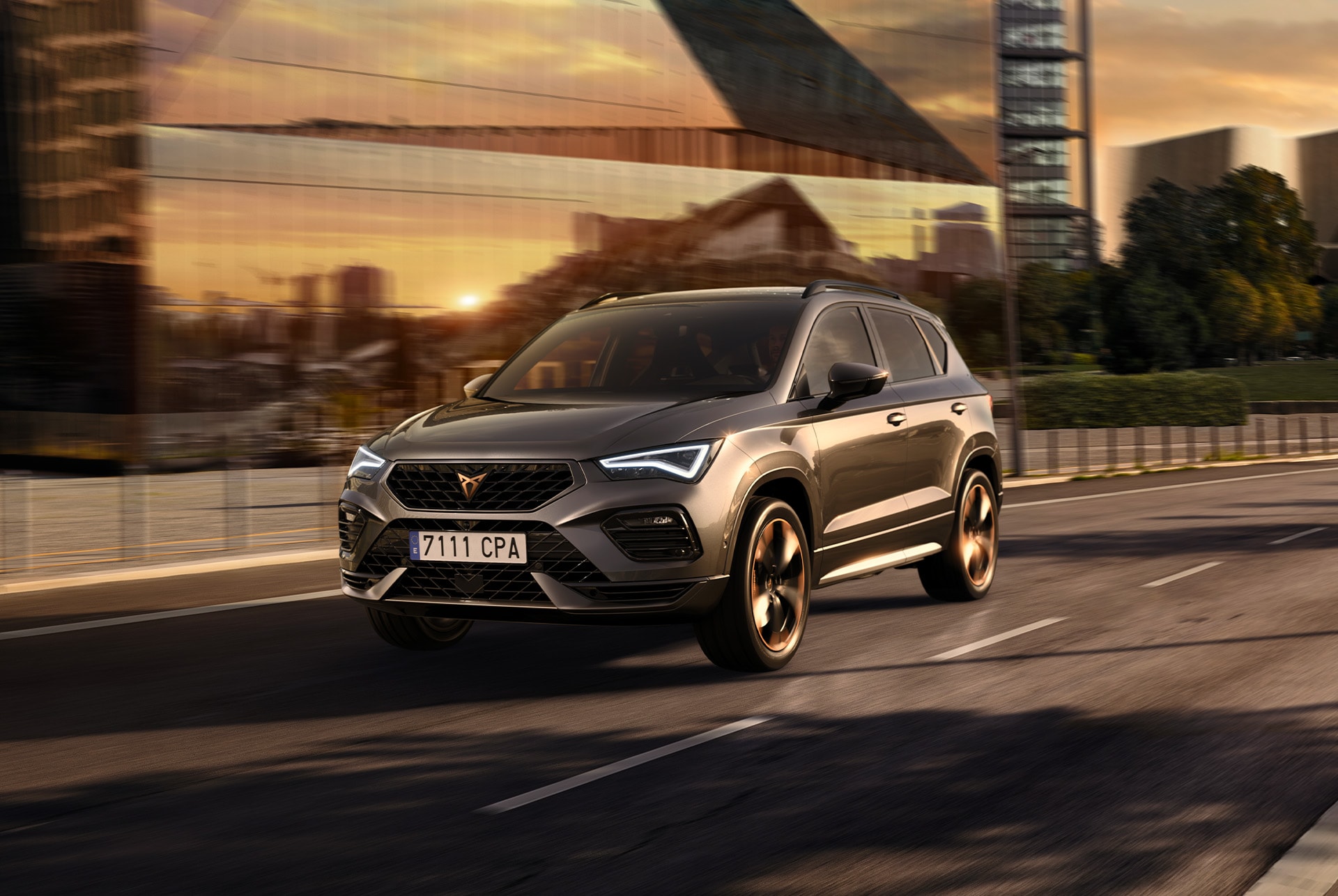 Un SUV CUPRA Ateca grigio viene raffigurato su uno sfondo bianco. La calandra pronunciata, i fari a LED e i cerchi in lega leggera con dettagli in rame sottolineano il design sportivo del veicolo.