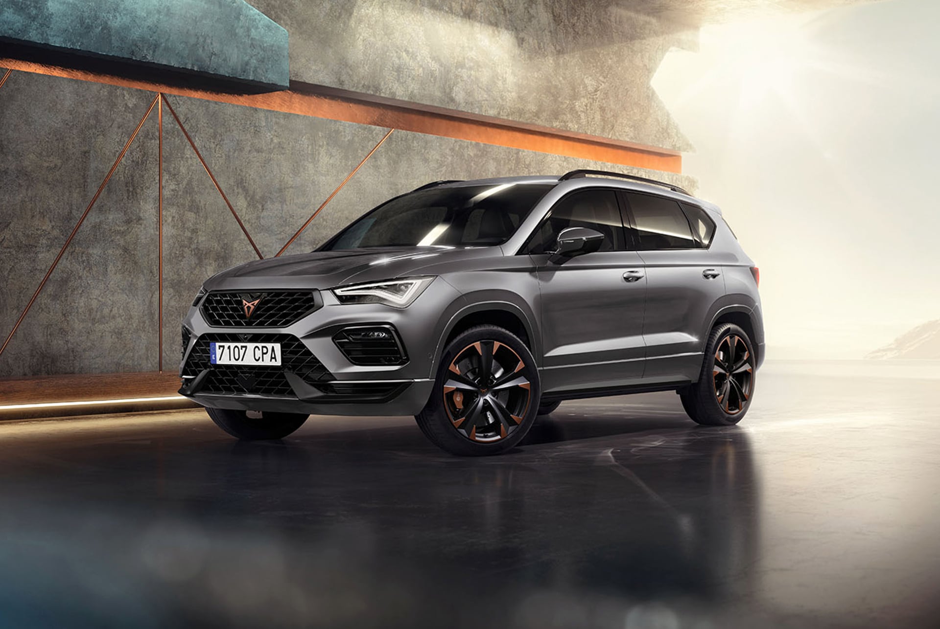 Une CUPRA Ateca 2024 en Graphite Grey, un SUV sportif et compact dans un environnement industriel moderne. Le design du véhicule se caractérise par des lignes aérodynamiques, des phares LED et des jantes en alliage léger marquantes aux accents cuivrés. L’arrière-plan montre un design géométrique des murs qui contraste avec le design élégant du véhicule.