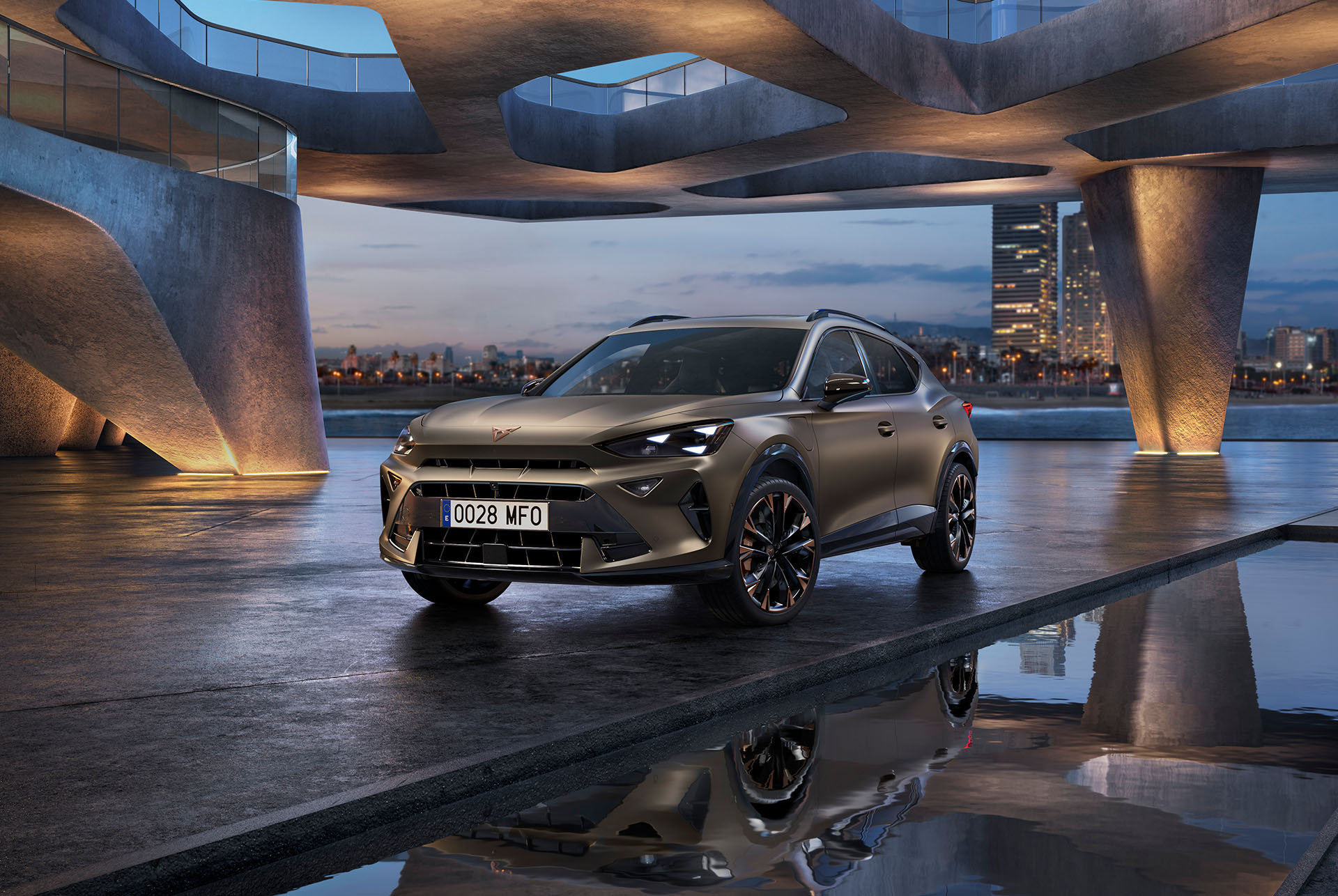 La CUPRA Formentor 2024 Century bronze mat est garée sur une promenade réfléchissante au bord de l'eau. Le nouveau véhicule sportif et aérodynamique est placé au centre du cadre. Le décor présente une architecture futuriste et l'horizon lumineux de Barcelone au crépuscule.