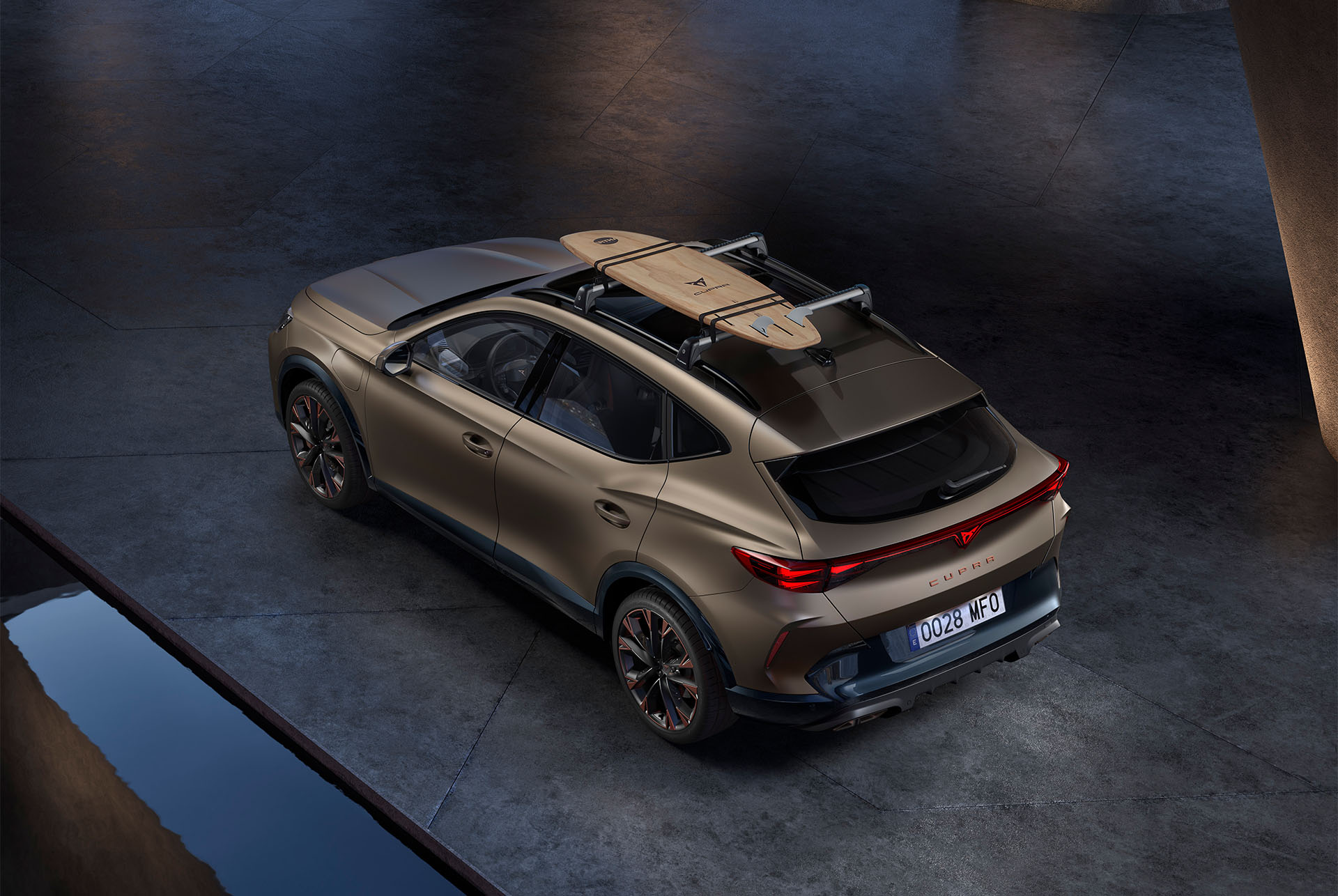 Vue d'oiseau de la CUPRA Formentor 2024 bronze mat du nouveau siècle avec un accessoire de support de planche de surf sur le toit de la voiture, voiture garée sur le béton.