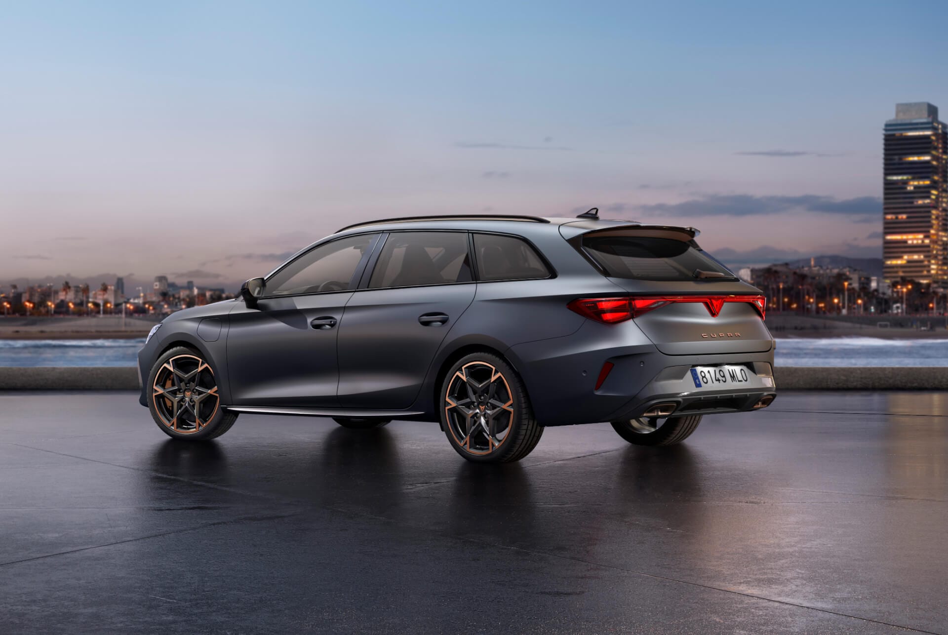 Der sportliche, neue 2024 Cupra Leon Sportstourer, parkiert auf Beton mit der in der Dämmerung beleuchteten Skyline der Stadt im Hintergrund. Das Fahrzeug wird in Matte Grey präsentiert.