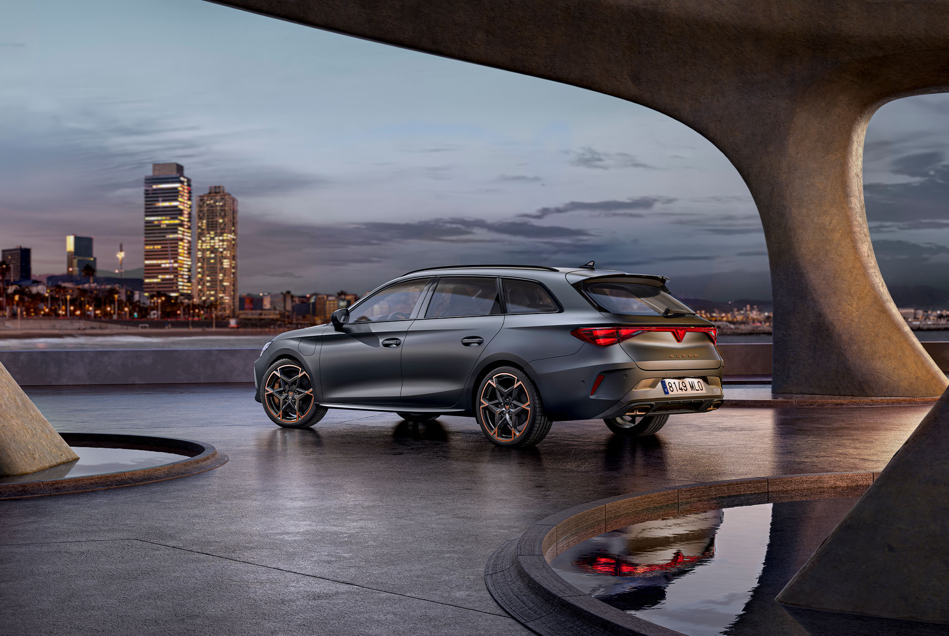 Vue arrière d’une nouvelle CUPRA Leon Sportstourer 2024, sportive et aérodynamique, en Matte Grey, garée sur une promenade au crépuscule. En arrière-plan, on aperçoit l’horizon lumineux de la ville.
