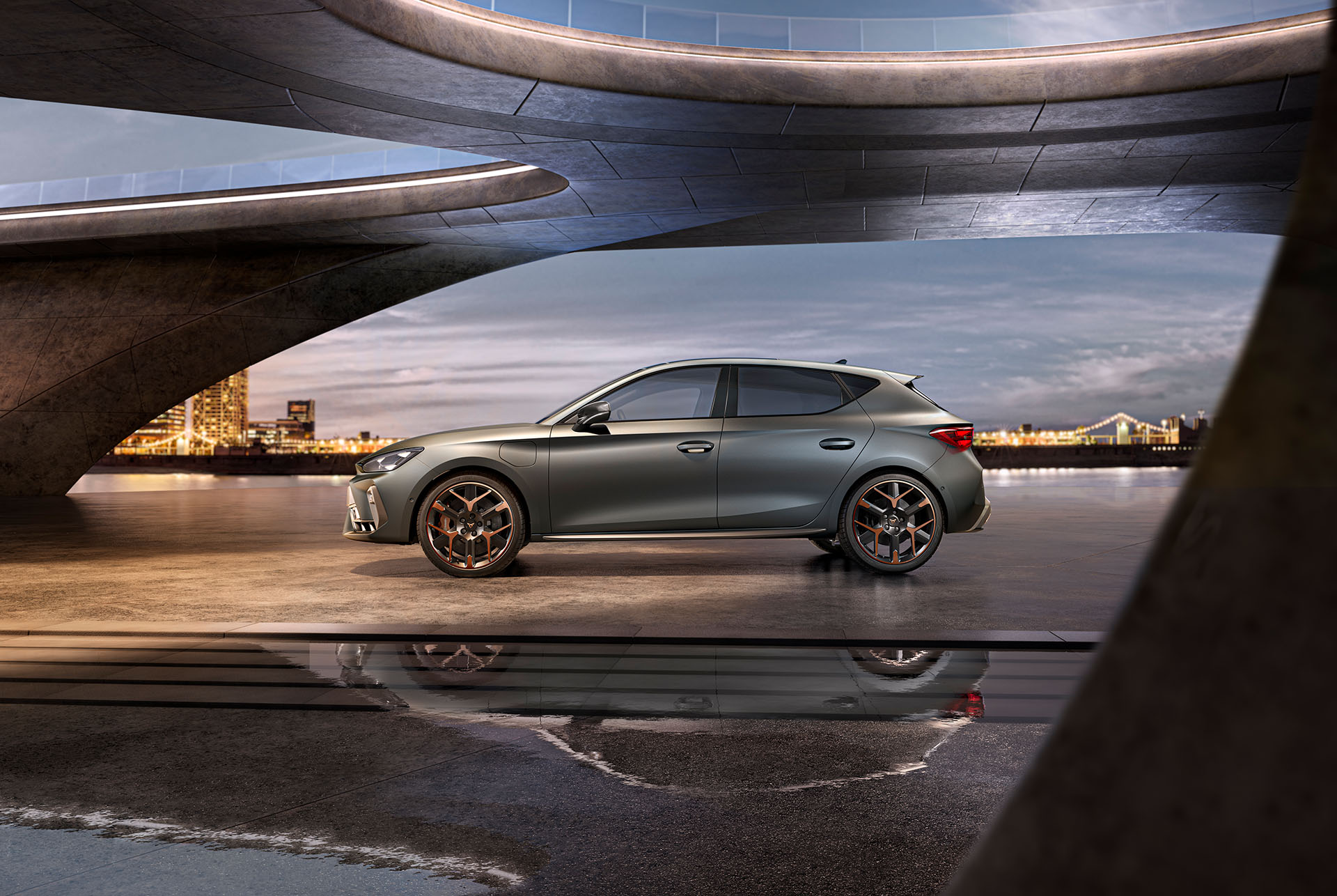 plan large de la nouvelle cupra leon 2024 vue de côté en gris garée sur du béton lisse sous une structure architecturale avec vue sur la mer et le paysage urbain, ciel nuageux. 