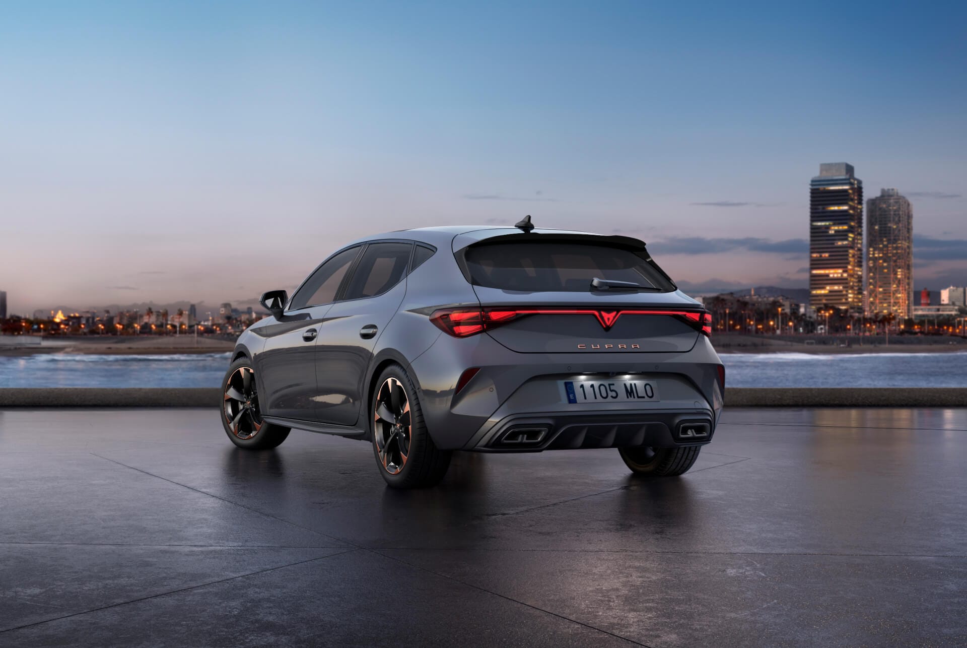 Heckansicht des neuen CUPRA Leon 2024 in Glossy Grey mit dynamischer Fahrwerksteuerung (DCC) sowie schwarz-kupferfarbenen Leichtmetallfelgen. Im Hintergrund die Stadt beim Sonnenuntergang.