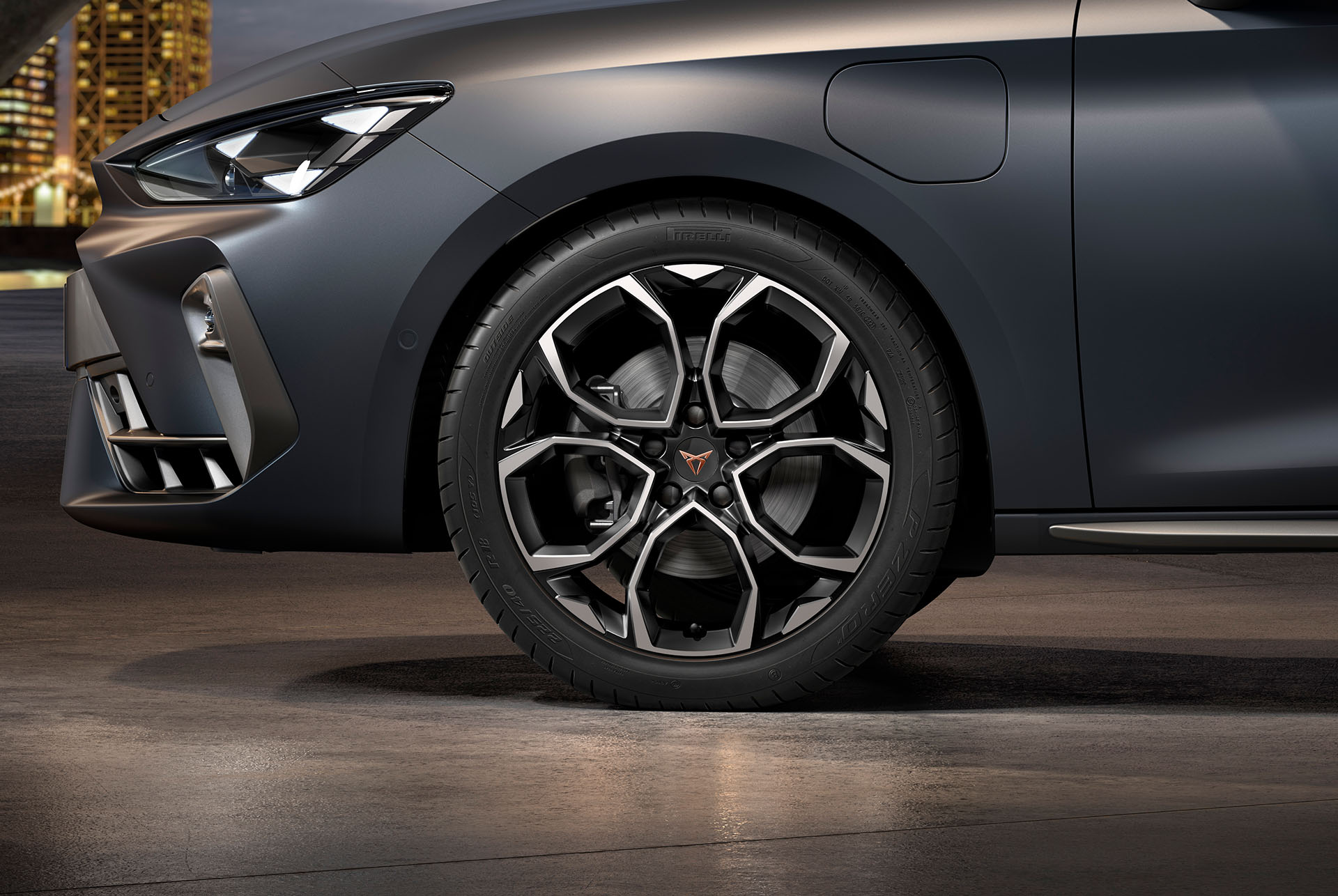Frontansicht der gefrästen schwarz-silbernen Windstorm-Leichtmetallfelge links für den neuen CUPRA 2024, Reifen, Signature-Scheinwerfer und graue Karosserie