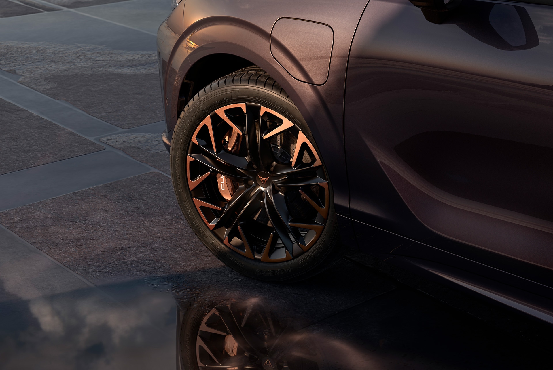 Jantes en alliage léger 20" «Hadron Copper» en noir avec accents cuivrés sur la nouvelle CUPRA Terramar. En arrière-plan, des pavés et une partie de la carrosserie sombre et brillante du véhicule.
