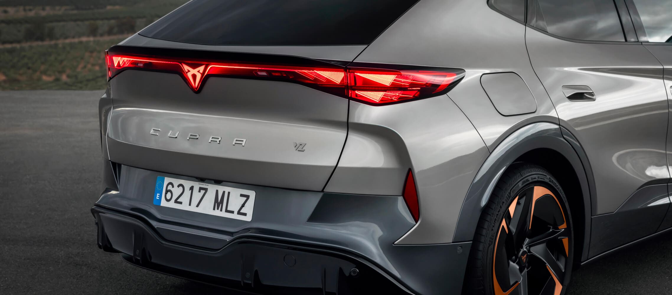 Firmenwagen, cupra tavascan in grau, Rückansicht mit kupferfarbenen Akzenträdern und Küstenlicht. 