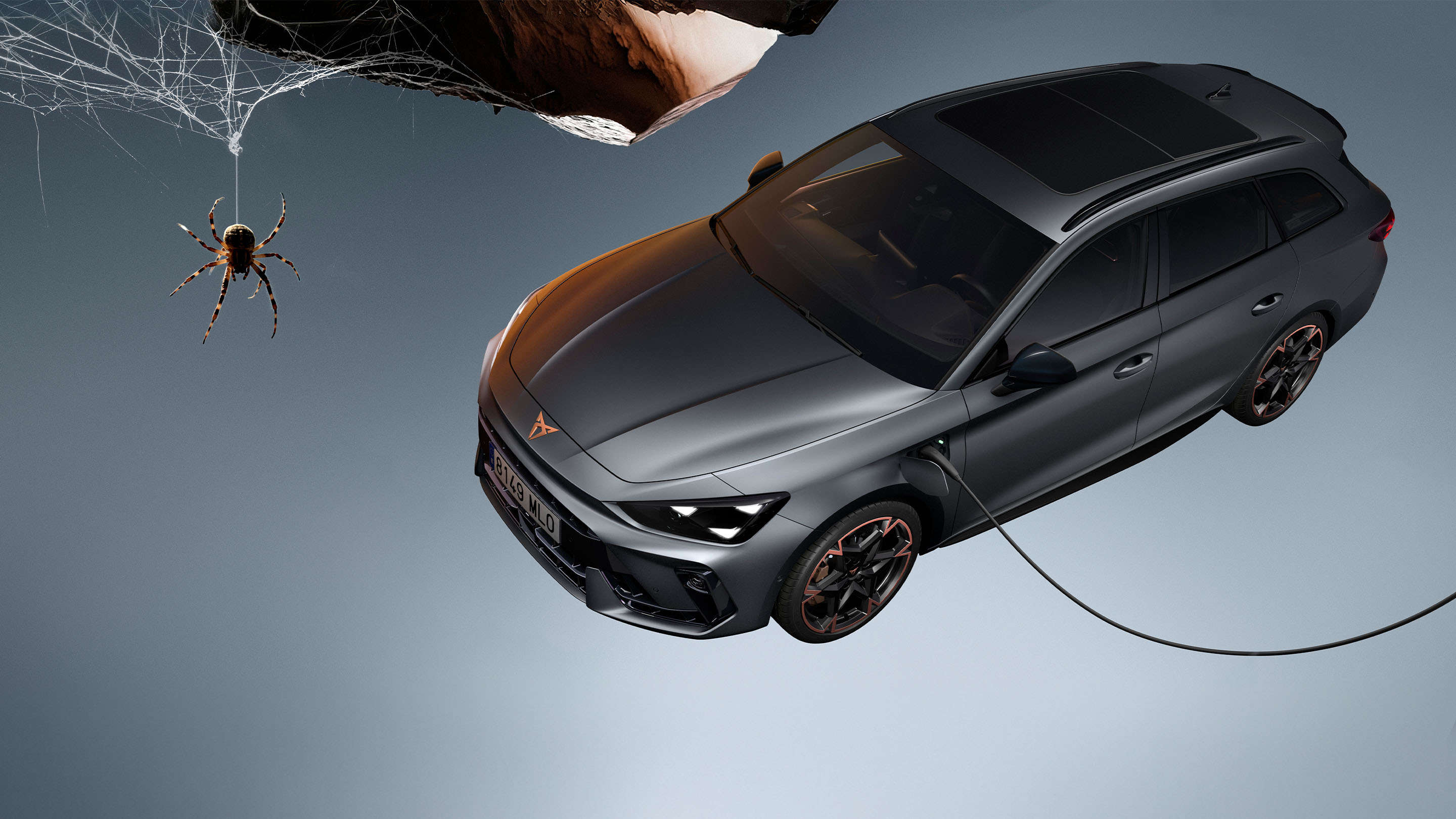 Vue grand angle de la nouvelle CUPRA Leon Sportstourer 2024 hybride sportive en Matte Grey, garée dans un environnement urbain devant de grandes fenêtres géométriques évoquant Gaudí.  